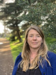 Amanda Moore standing on a path against a backgrop of green trees and a field with 