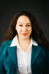 Headshot of poet Angela Chaidez Vincent, wearing teal-colored velvet blazer and white blouse against a solid dark background